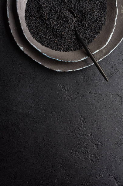 Black sesame seeds in black ceramic plates on a dark old vintage background. Rustic style. Top view. - Foto, Imagem