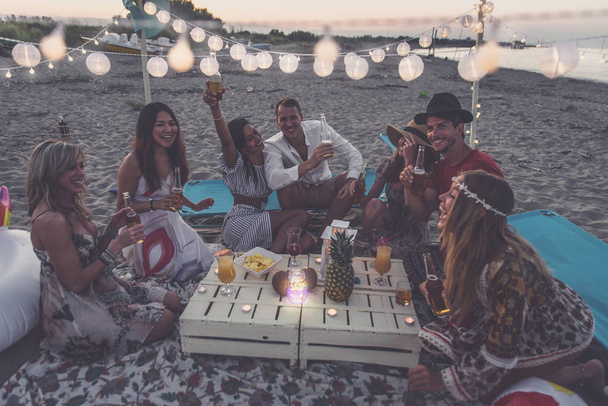Group of friends making party on the beach at sunset time - Foto, imagen