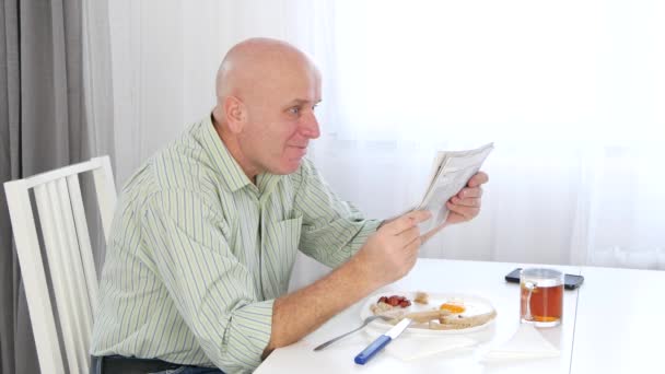 Relaxed Businessman Taking Breakfast in Dining Room and Reading Gazette News. - Materiaali, video