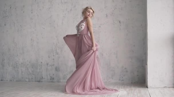 The charming blonde in evening dress is spinning and her dress is fluttering. portrait of an attractive girl with a festive make-up and hairdo. - Footage, Video