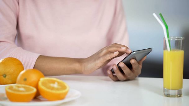 Multiracial girl using smartphone in kitchen, oranges on table, healthcare food - Foto, Imagem