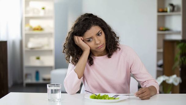 Sad lady in front of green salad plate and glass of water on table, weight loss - Foto, Imagen