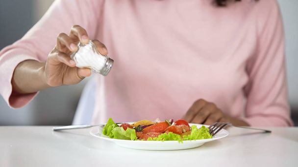 Woman adding too much salt to her food, unhealthy eating, dehydration problems - Photo, image