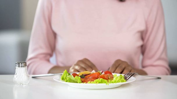 Fresh vegetable salad and saltshaker on dinner table, woman having lunch at home - Foto, afbeelding