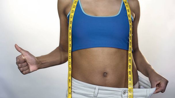 Fit woman wearing oversized pants, showing thumbs-up, weight loss result, diet - Foto, afbeelding