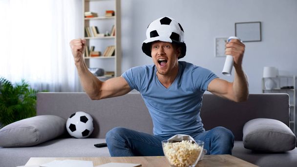 Football supporter in fan hat sincerely rejoicing to scored kick at last minutes - 写真・画像