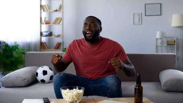 Cheerful afro-american man watching sports tournament, dangerous moment, point - Fotó, kép