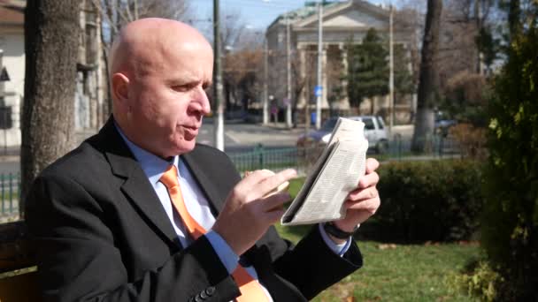 Businessman Sitting on Park Bench Eat Sandwich and  Read Daily Newspaper. - Filmati, video