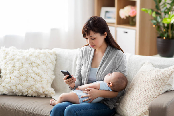 mother with sleeping baby and smartphone at home - 写真・画像