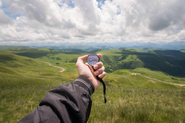 A mans hand of a tourist with an authentic compass on the background of a mountain road landscape - Fotó, kép