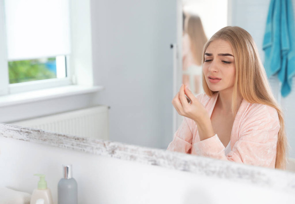 Молодая женщина с проблемой потери ресниц смотрит в зеркало в помещении
 - Фото, изображение