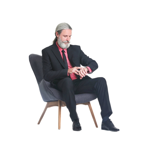 Knappe bebaarde volwassen man in pak zitten in fauteuil op witte achtergrond - Foto, afbeelding