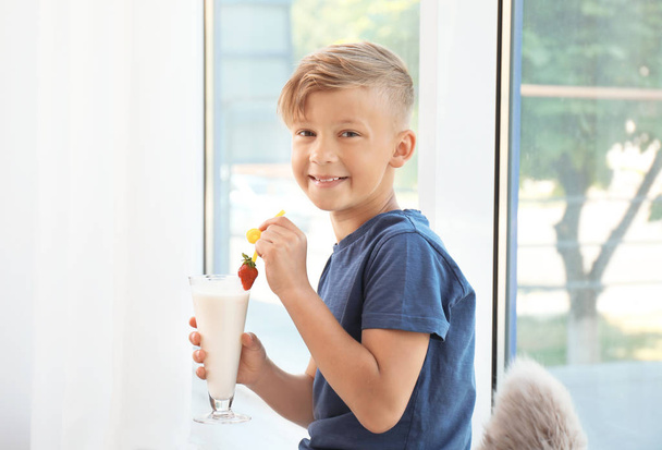 Little boy with glass of milk shake near window indoors - Foto, Bild