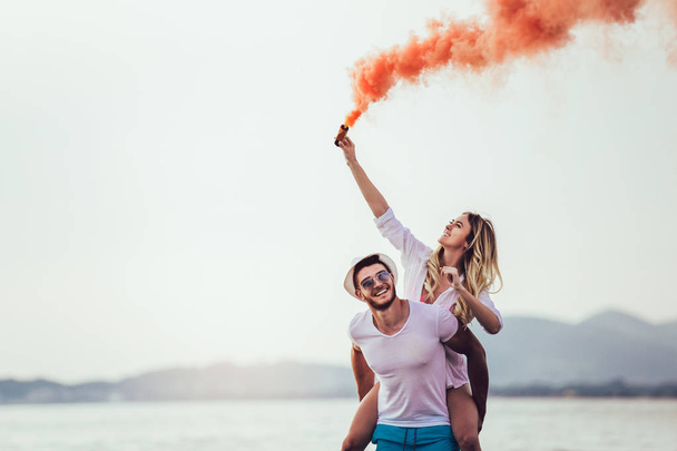 Hermosa pareja joven con bomba de humo en la mano está de pie al aire libre en el fondo dorado del verano
. - Foto, imagen
