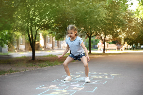 Little child playing hopscotch drawn with colorful chalk on asphalt - Фото, зображення