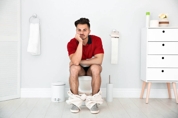 Young man sitting on toilet bowl at home - Fotoğraf, Görsel