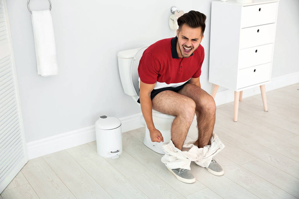 Young man suffering from diarrhea on toilet bowl at home - Fotoğraf, Görsel
