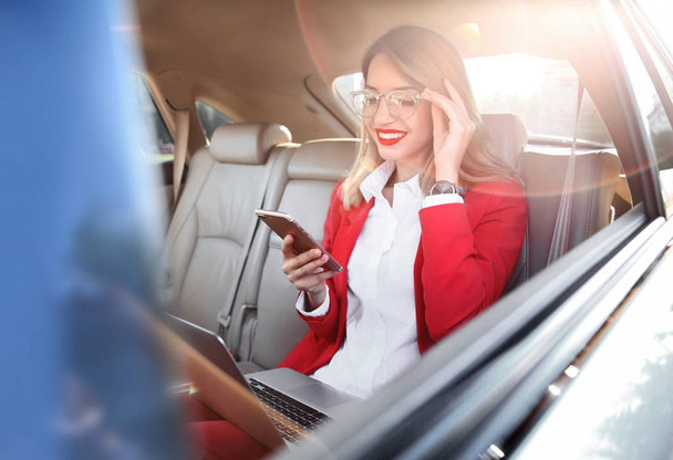 Young businesswoman with smartphone and laptop in car - Foto, immagini