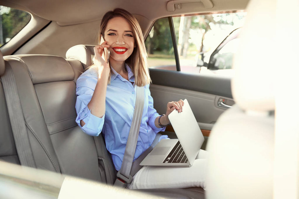Young businesswoman with smartphone and laptop in car - Foto, imagen