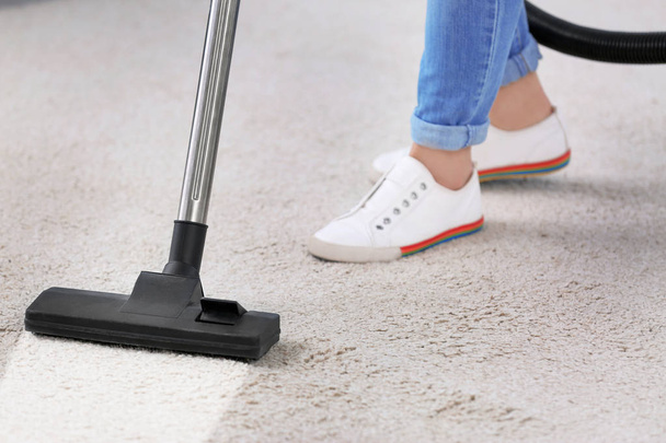 Woman removing dirt from carpet with vacuum cleaner indoors, closeup - Photo, image