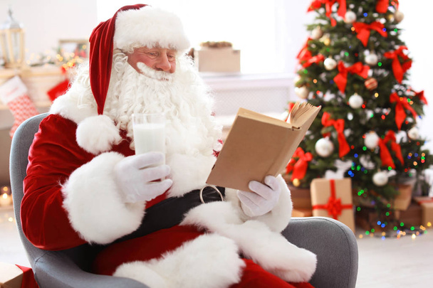Authentic Santa Claus with glass of milk reading book indoors - Фото, зображення