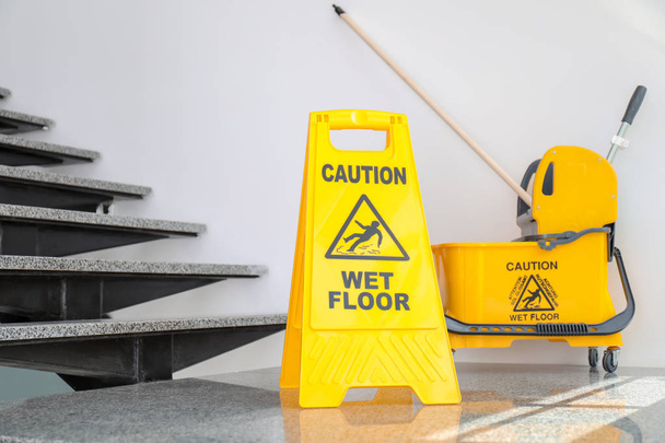 Safety sign with phrase Caution wet floor and mop bucket near stairs. Cleaning service - Zdjęcie, obraz