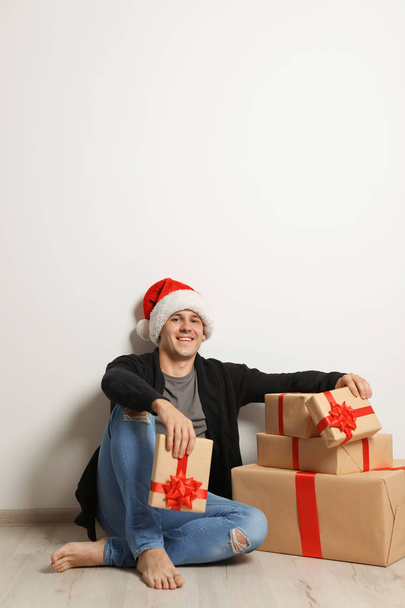 Young man with Christmas gifts near white wall - Valokuva, kuva