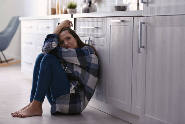 Depressed young woman sitting on floor in kitchen - Zdjęcie, obraz