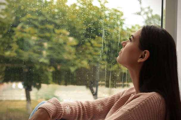 Fiatal szomorú nő ül otthon ablak közelében - Fotó, kép