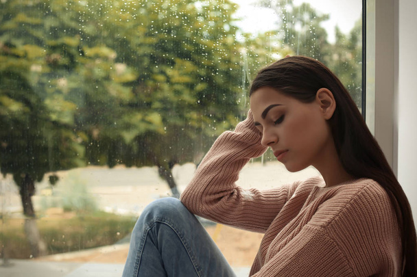 Young sad woman sitting near window at home - Zdjęcie, obraz