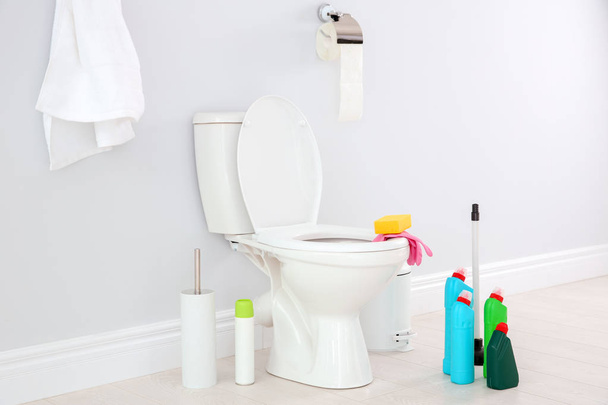 Ceramic toilet bowl, bottles of detergent and cleaning supplies in modern bathroom - Photo, Image