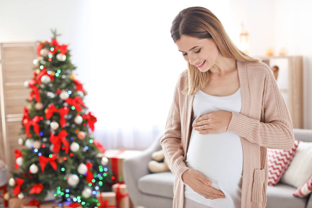 Счастливая беременная женщина в комнате, украшенной к Рождеству
 - Фото, изображение