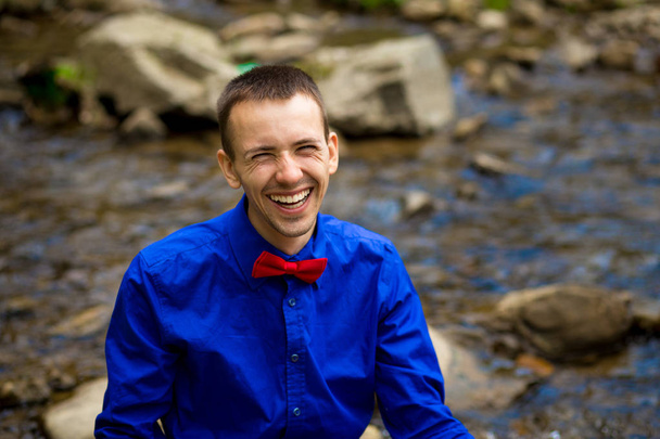 Πορτρέτο των νέων χαμογελώντας όμορφος άνδρας στο μπλε πουκάμισο κοντά στο δάσος του ποταμού. Αντίληψη των συναισθημάτων - Φωτογραφία, εικόνα