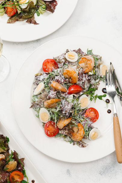 Green salad with tomatoes, quail eggs and roasted shrimps on white plate - Photo, Image