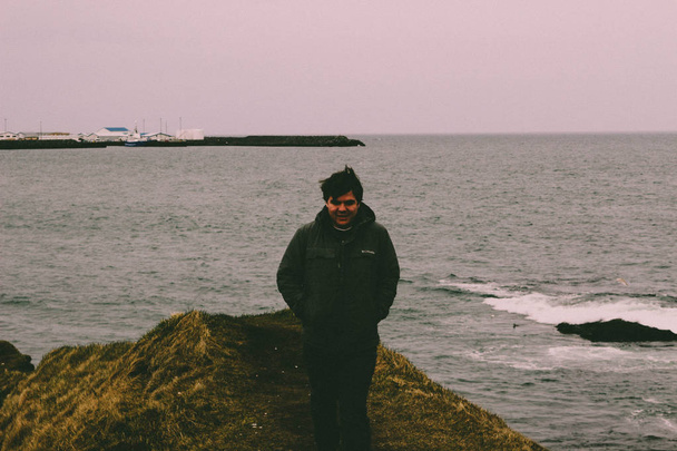 Jovem do sexo masculino 20-25 abraçando a natureza da Islândia em fotos dramáticas fora do oceano. Céu muito cinzento e deprimente
 - Foto, Imagem