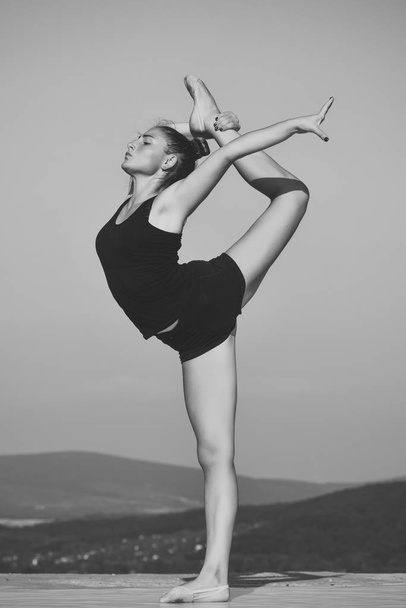 training in athletics. Woman gymnast in black sportswear in yoga pose. - 写真・画像