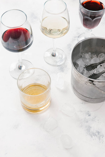 Bril met rode en witte wijn, glas whisky en pot met ijsblokjes op witte concrete achtergrond - Foto, afbeelding
