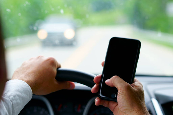 Don't text and drive! A man is texting with a finger while a car is arriving in front.  Focus on the finger, focus on telephone, focus on the car coming. - 写真・画像