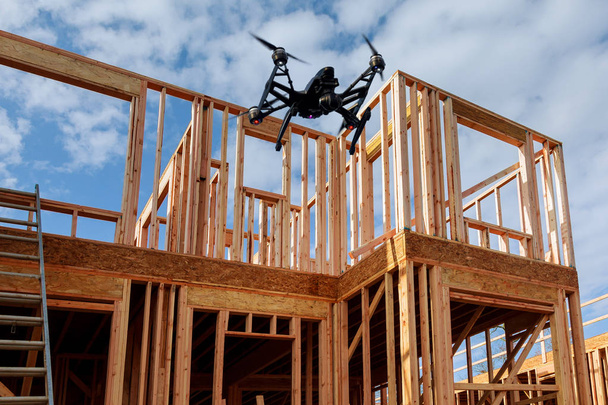 quadcopter drone noir avec caméra survolant la construction résidentielle maison encadrant contre un La maison est nouvelle dans la toiture en bois
 - Photo, image