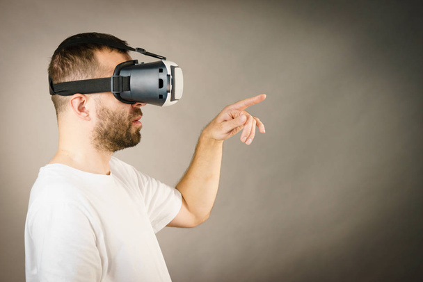 Adult short bearded guy exploring virtual reality wearing VR goggles being into technology pointing at something. Studio shot side view. - Foto, Bild
