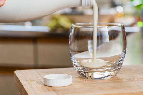 Kézi szakadó friss kefir probiotik ital fehér üveg tiszta üveg konyhaasztalon - Fotó, kép