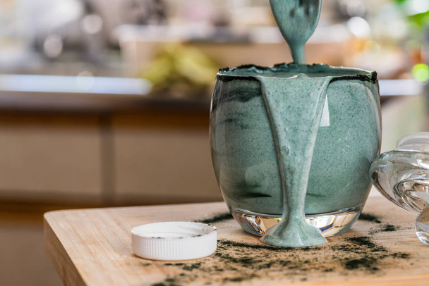Vista close up bebida probiotik kefir fresco em vidro transparente misturado com pó espirulina verde na mesa da cozinha
 - Foto, Imagem