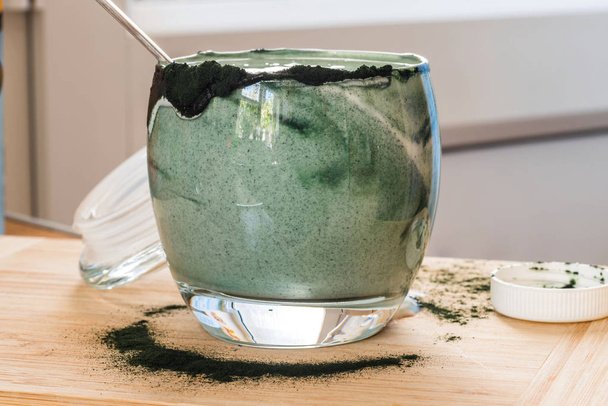 Вид крупным планом свежий кефир пробиотик напиток в прозрачном стекле смешанный с зеленой спирулиной порошок на кухонном столе
 - Фото, изображение