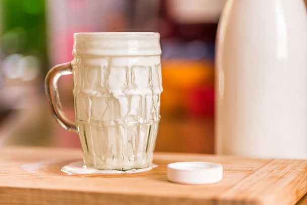 Close-up weergave verse kefir probiotik drankje voortgekomen uit overvolle leeg glas op keukentafel - Foto, afbeelding