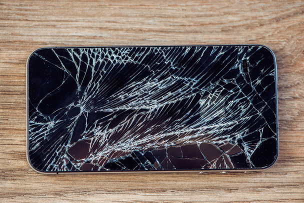 Smartphone display with broken glass on a wooden table - Foto, immagini