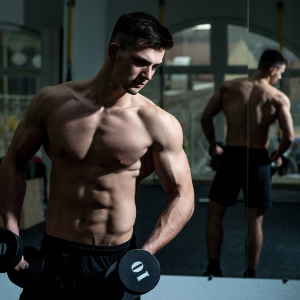Sportsman, athlete with muscles looks attractive. Man with torso, muscular macho and his reflexion in mirror background.Man with nude torso in gym enjoy his sporty lifestyle. Sport and gym concept - Foto, afbeelding