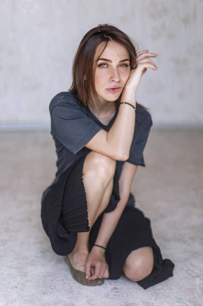 attractive woman wearing blue t-shirt and black pants while sitting on floor in comfort pose - 写真・画像