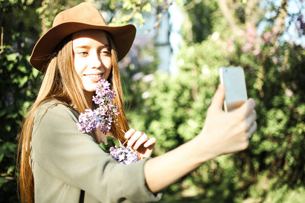 Piękna dziewczyna czy selfie w brązowy kapelusz z gałązką fioletowy liliowy. - Zdjęcie, obraz