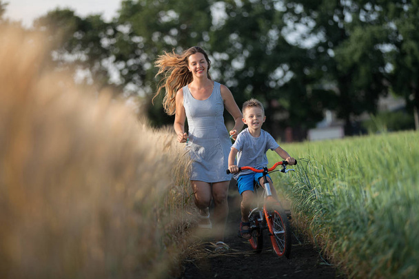 Mutter und Sohn verbringen Zeit miteinander. Der Junge fährt Fahrrad, und das Mädchen rennt mit. Familie auf dem Land. - Foto, Bild