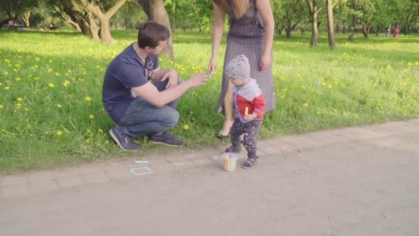 Menino com pais jovens pinta giz no asfalto. Movimento lento
 - Filmagem, Vídeo